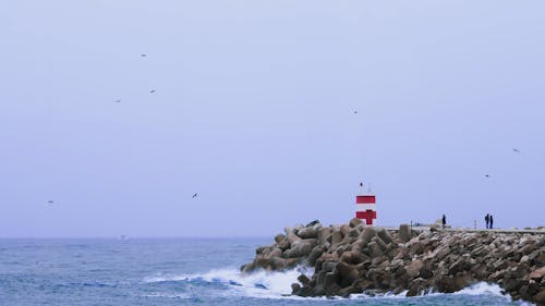 Small lighthouse at Nazaré, Portugal. Stormy dark weather with silhouette of bystanders and seagulls flying by