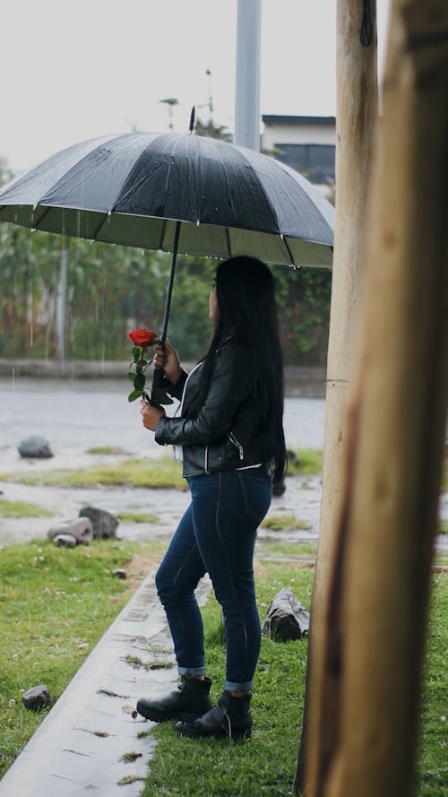A girl in a raining rain with a rose and a umbrella