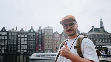a man with a backpack and glasses is giving the thumbs up