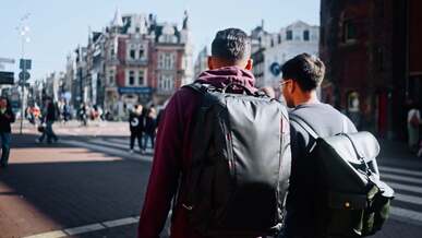 two men walking down a city street with a backpack