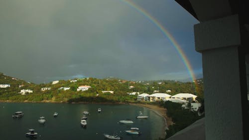 Full vibrant rainbow over quiet harbor and boats