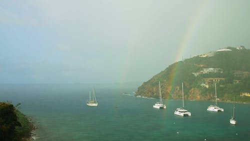 Sailboats anchored in cozy harbor during rain shower and rainbow