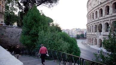 a man walking down a sidewalk in front of the roman colossion