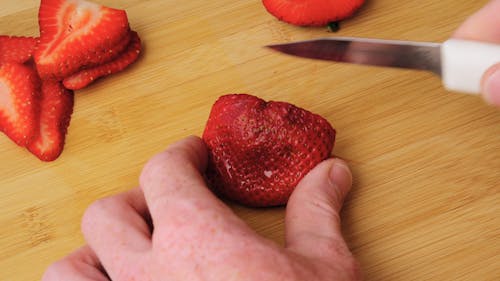 Person Slicing Fresh Strawberries On A Chopping Board