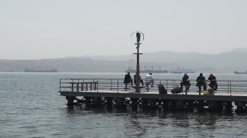 People Relaxing on a Dock with Ships in the Background