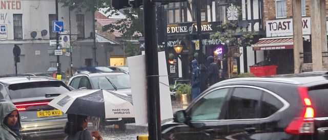 A busy rainy street scene in London with people and cars bustling under umbrellas.