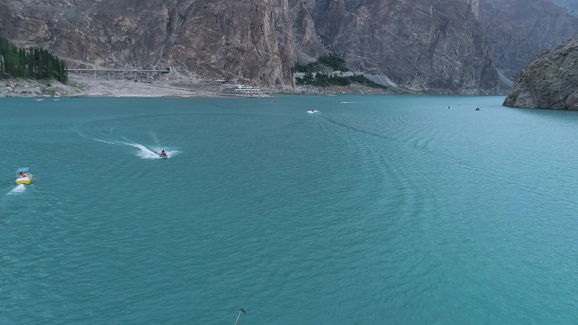 Drone flight over the Hunza valley, a long blue river below with boats ...