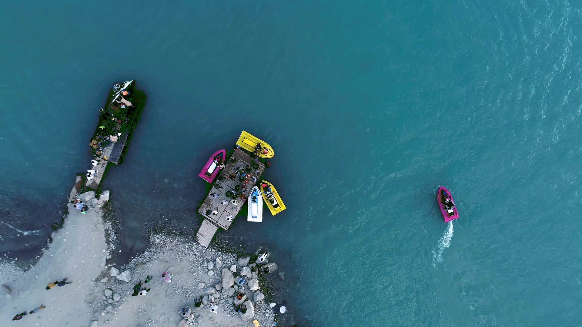 Drone flight over the Hunza valley, a long blue river below with boats ...