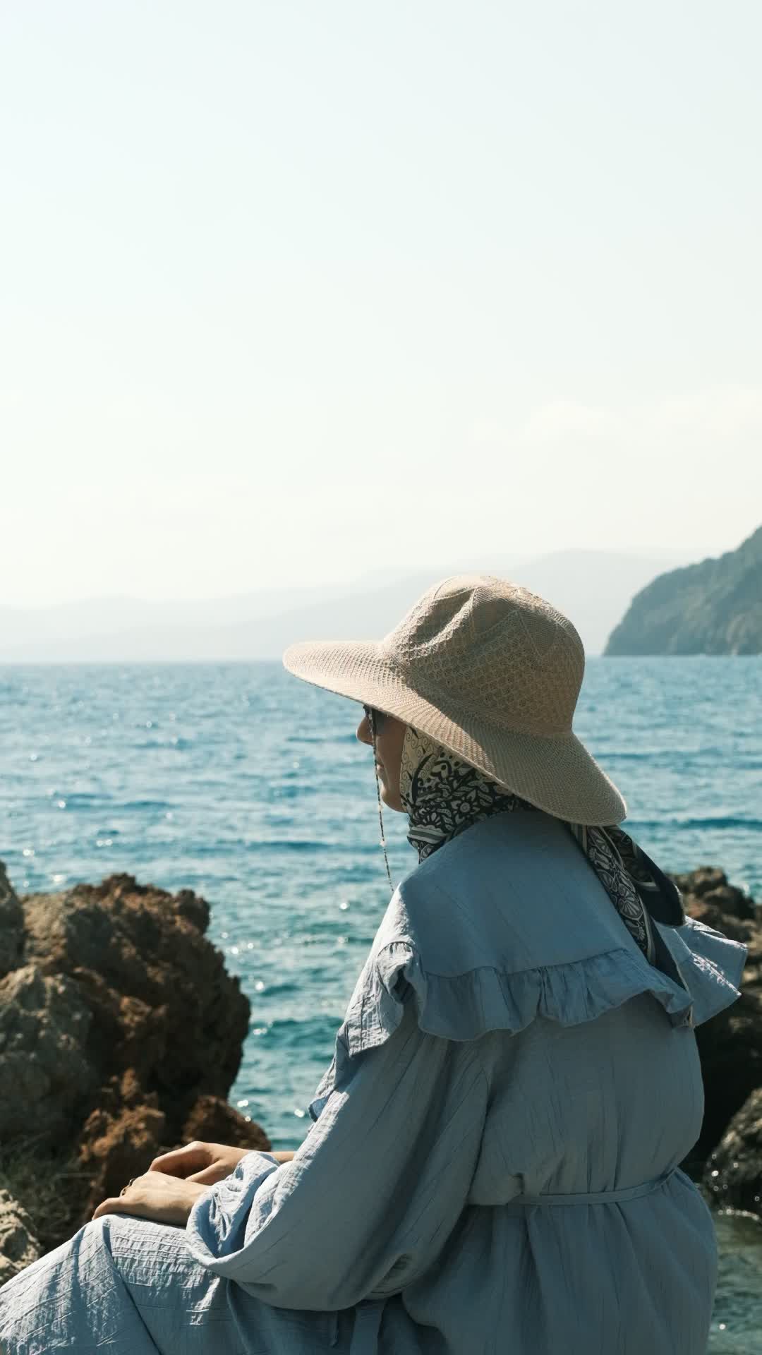 A woman in a hat sitting on rocks by the ocean Free Stock Video Footage ...