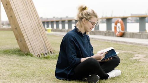 Женщина читает книгу, сидя на траве