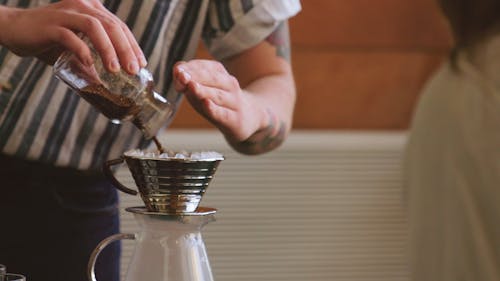 뜨거운 양조 커피를 만들기 위해 주석 컵 필터에 원두 커피를 붓는 남자