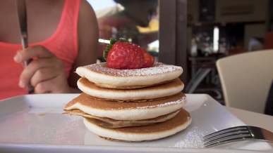 pouring syrup on a pile of pancakes with a strawberry fruit topping