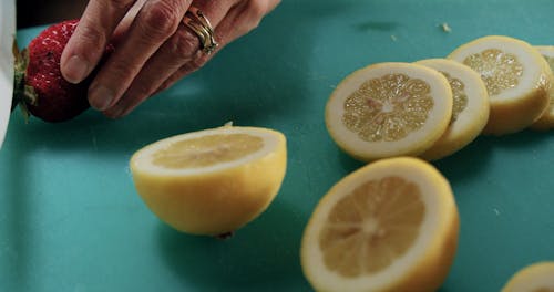 Slow Motion Footage Of A Person Slicing Fresh Strawberries And Lemons On A Blue Cutting Board