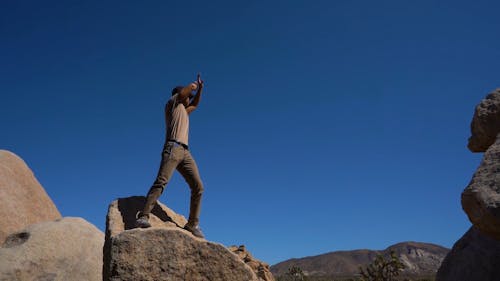 신호를 보내거나주의를 요청하는 바위 위에 서있는 남자의 낮은 각도 영상