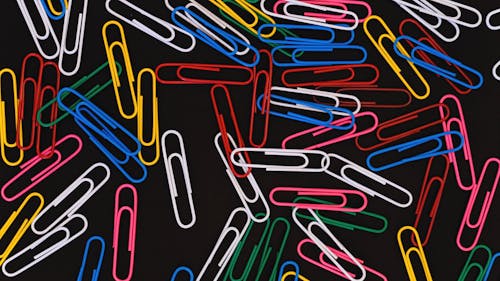 Paper Clips Of Different Colors Moving On Top Of A Black Surface