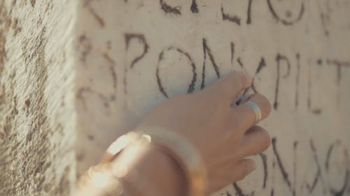 Slow motion footage Of A Woman"s Fingers Touching A Stone wall With Carved Ancient Script