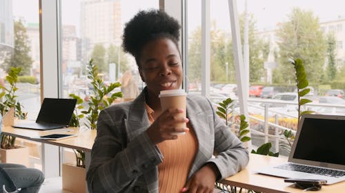 Une Femme Appuyée Sur Une Table De Comptoir Avec Des Ordinateurs Portables En Profitant D'un Verre Dans Une Tasse De Café à Emporter