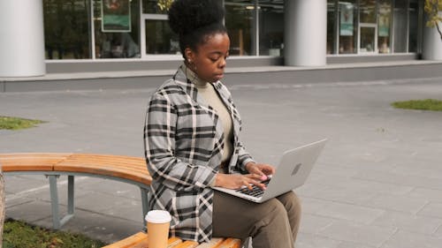 A Woman Seated On An Outdoor Bench Works On Her Laptop