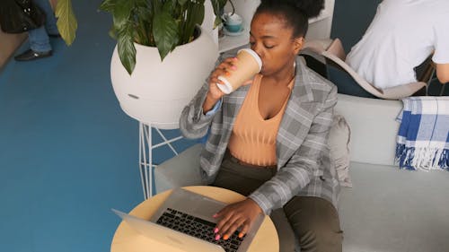 A Woman Drinking On A Cup Of Coffee While Working On Her Laptop