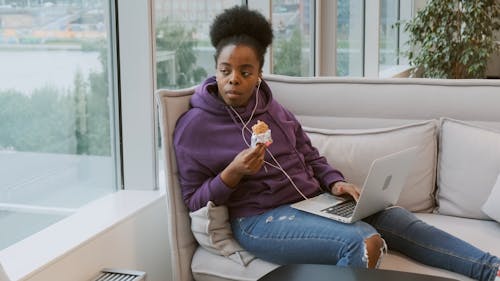 A Seated Woman Eating A Candy Bar While Having A Her Laptop On Her Lap