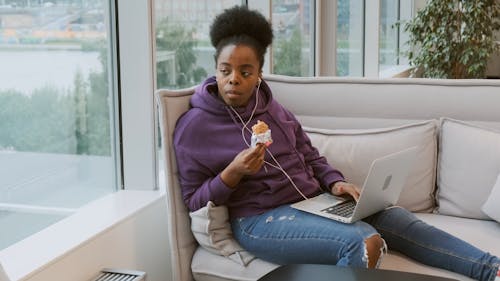 Eine Sitzende Frau, Die Einen Schokoriegel Isst, Während Sie Ihren Laptop Auf Ihrem Schoß Hat