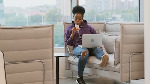 ノートパソコンで快適に座っている間にキャンディーバーを食べる女性