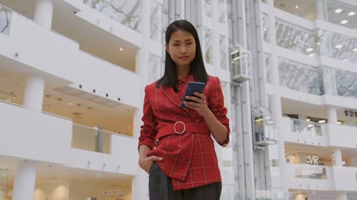 A Standing Woman With A Cellphone On Hand Exhibits A Smile