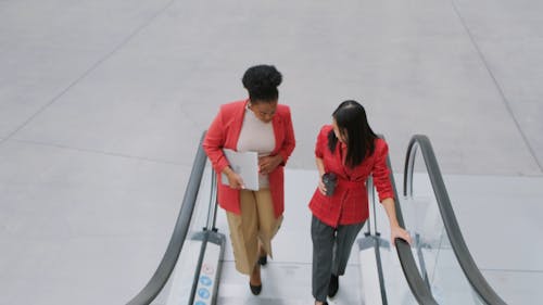 Two Women Having A Conversation While On An Escalator