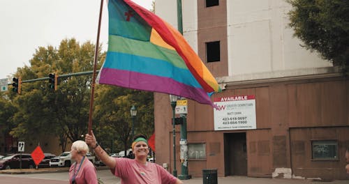 通りをパレードしながら虹色の旗を振る男