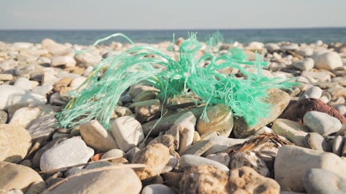 躺在海灘岸邊的卵石岩石上的一塊塑料繩