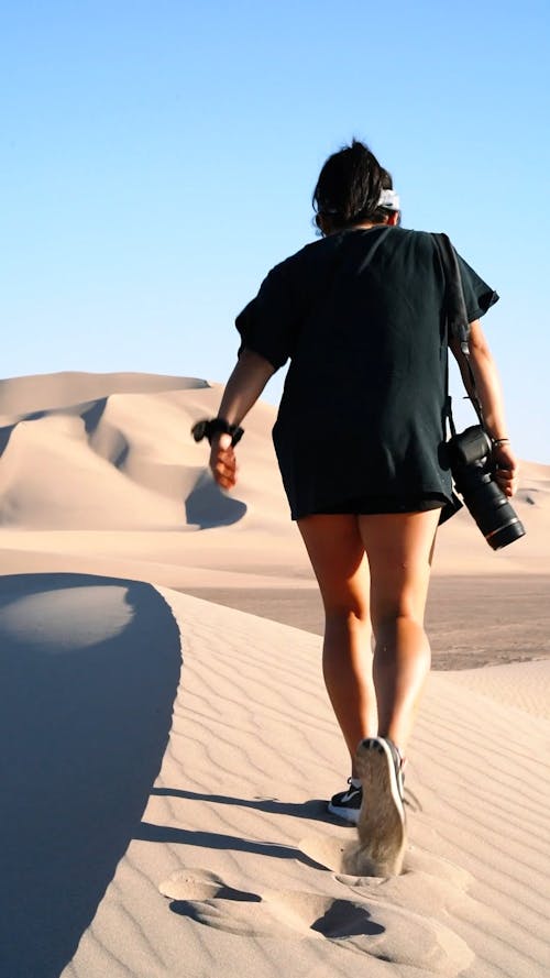 A Woman Walking In The Sandy Desert With Camera On Hand