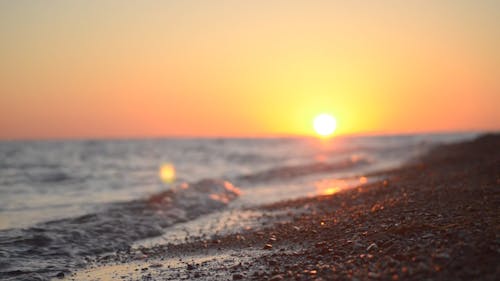 Ground Level Footage Of Waves Breaking On The Shore With The Sun Setting In The Horizon