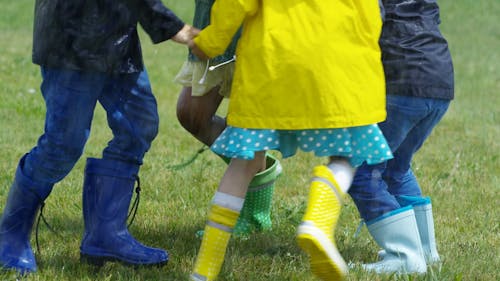 Дети в водонепроницаемых сапогах играют на траве под дождем