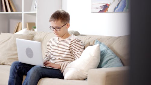 一個男孩在客廳沙發上使用一台筆記本電腦