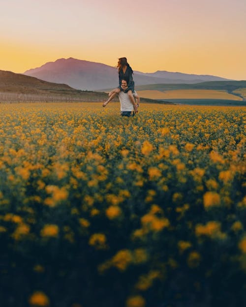 A Man Carrying A Woman Over His Shoulders On A Field Of Flowers