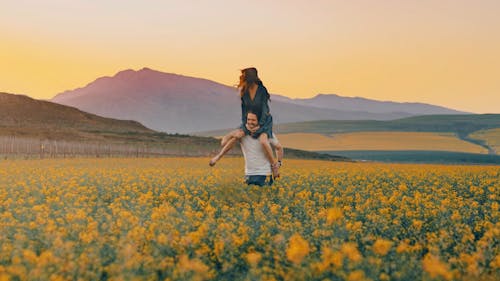 A Man Carrying A Woman On His Shoulders Having Fun In A Flower Field 