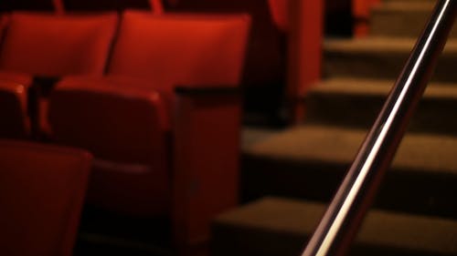 Panning Footage Of Rows Of Red Vinyl Chairs Along The Aisle Stairs Of A Movie Theater