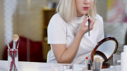 A Woman Applying Lip Color Using A Lip Brush