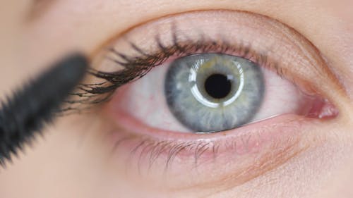 A Woman Putting On Mascara On Her Left Eyelashes