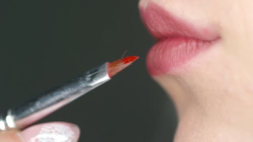 A Woman Brushing On Red Color Lipstick On Her Lips
