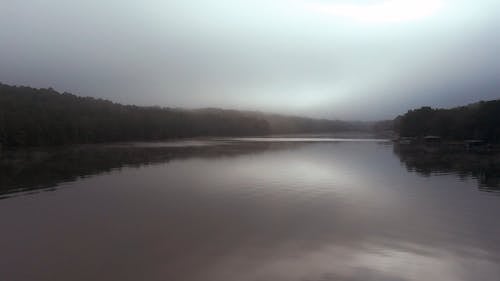 A Lake With Calm Waters On A Foggy Day