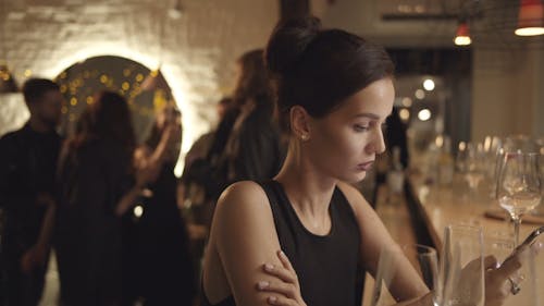 A Woman Sitting At A Bar With Group Of People Dancing Behind