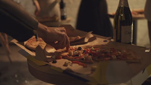 A Person Grads A Slice Of Pizza In A Box