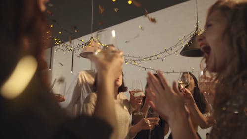 People In A Party Raising Their Glasses For A Toss While Confetti Are Falling