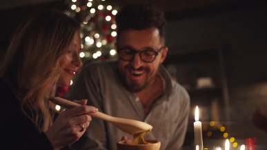 a woman jokingly let a man taste the dipping using a large wooden spoon