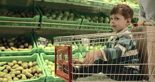 Een Jongen Geplaatst In Een Duwkar Die Door De Groentesectie In Een Kruidenierswinkel Gaat