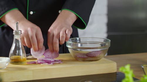 A Person Tossing Onion Slices On A Crystal Bowl With Olive Oil