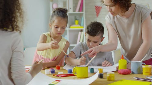 Bambini Che Fanno Alcuni Dipinti Di Carta Sotto La Supervisione Degli Adulti