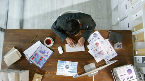 Мужчина использует свой компьютер для записи данных о документах на своем столе