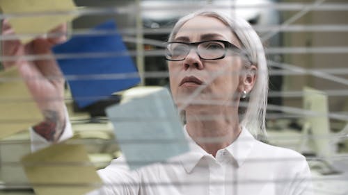 A Woman Checking Notes On Paper Pads Stick To A Glass Panel